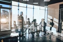 Conference being held in a modern office with glass walls. Several people inside are obscured by glares on the glass from the sun.