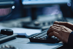 A close-up on a person's hands typing on a keyword at a computer